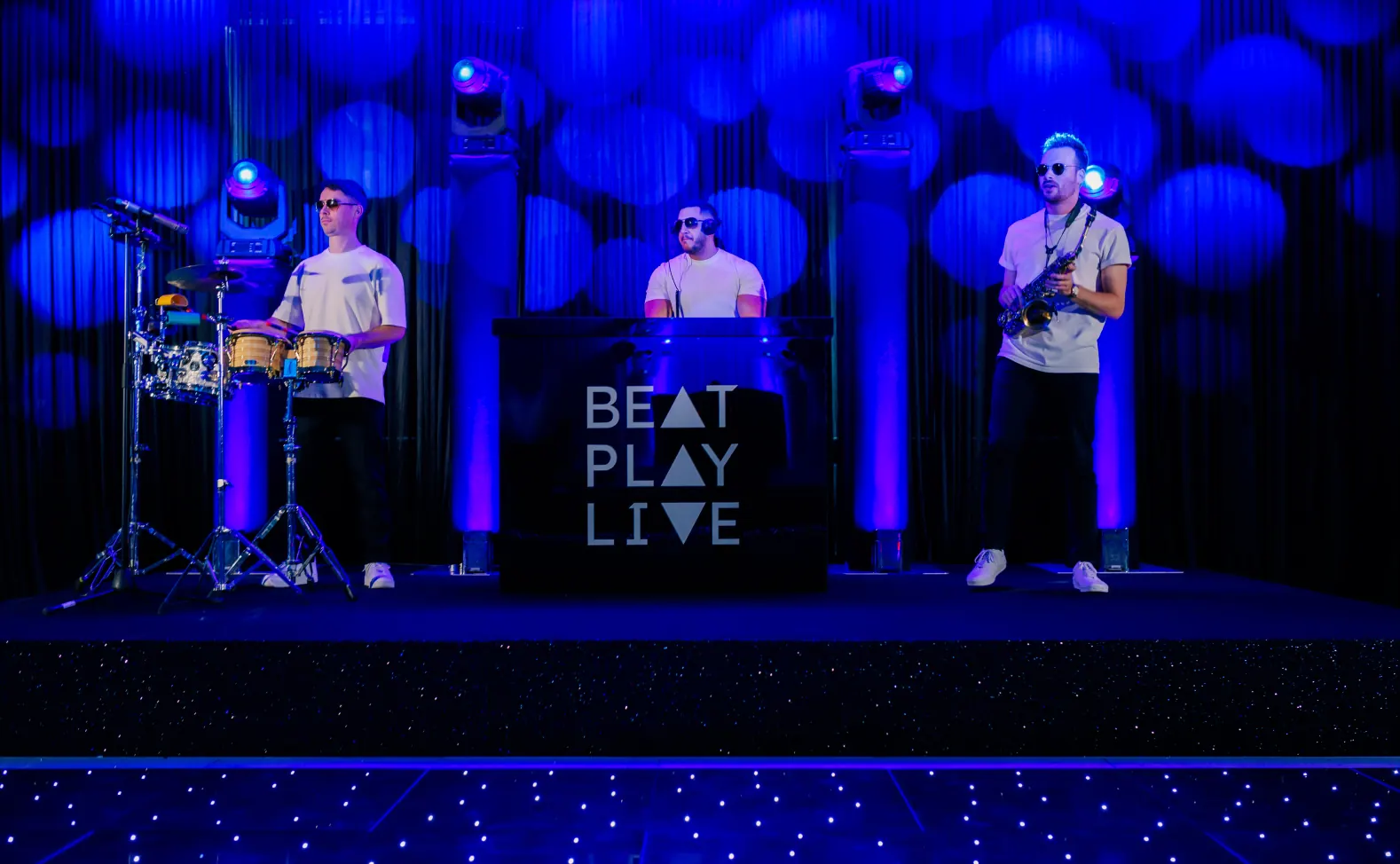 BeatPlayLive on stage: percussion, DJ and saxophone under blue lights